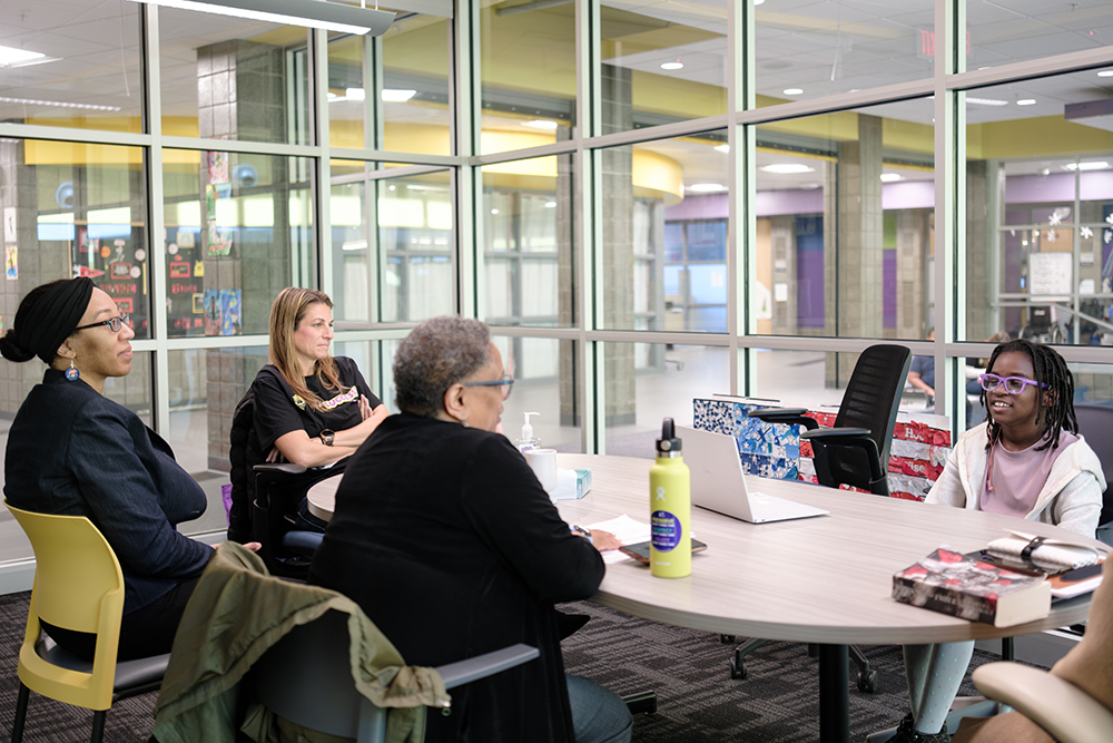 IMpact People seated around a table in a glass-walled room